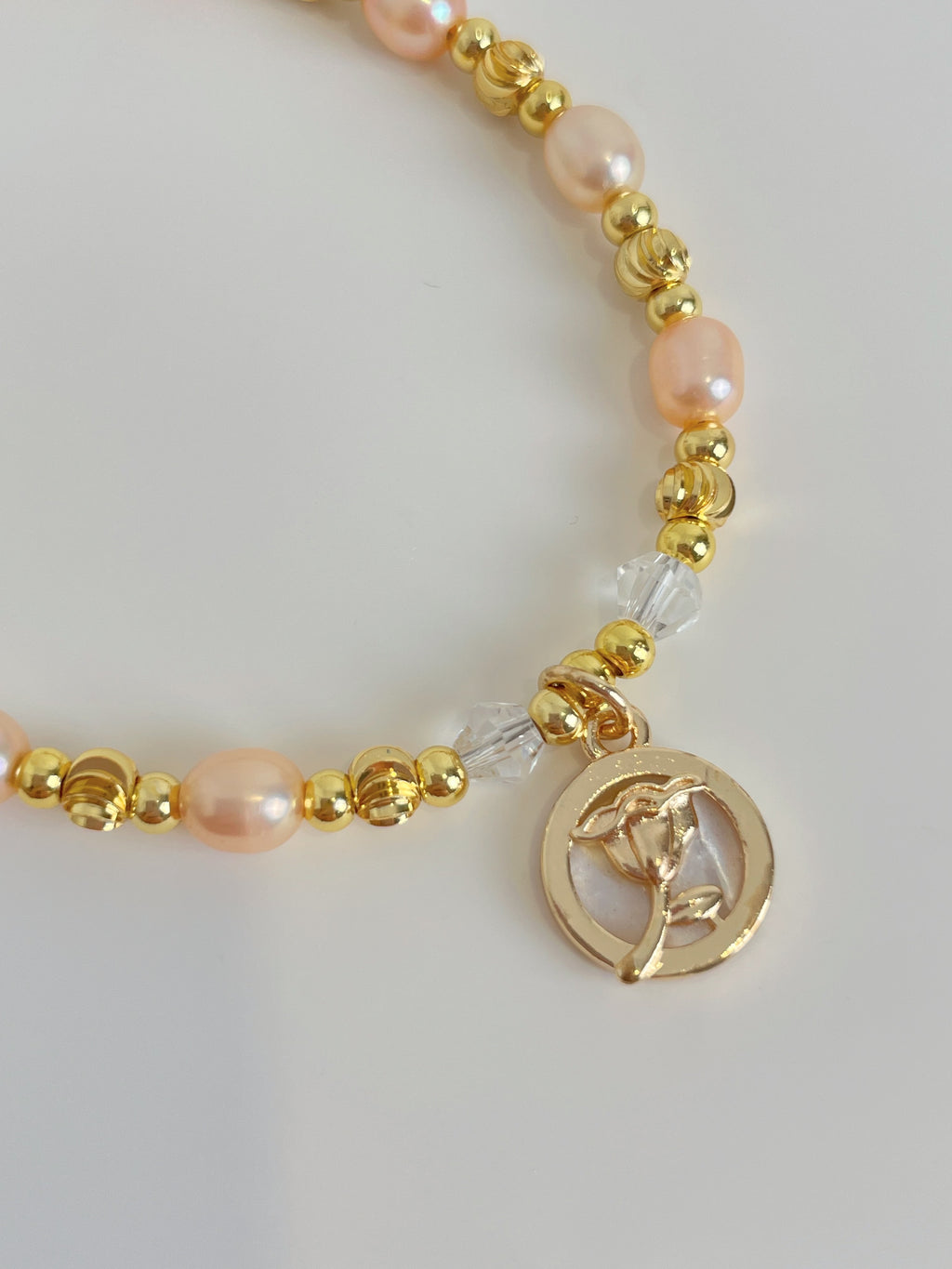 Delicate pink freshwater pearl bracelet featuring gold accents and a charm with a floral design.