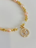 Delicate pink freshwater pearl bracelet featuring gold accents and a charm with a floral design.