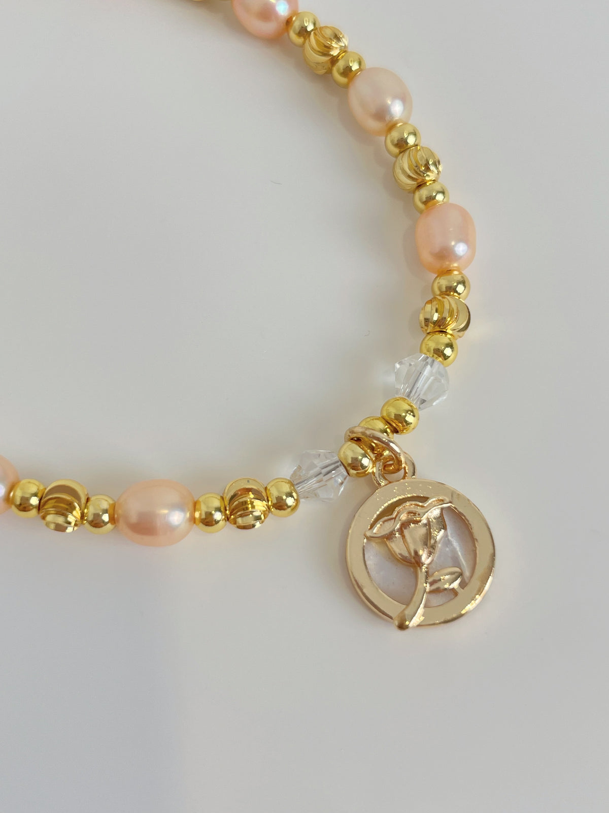 Delicate pink freshwater pearl bracelet featuring gold accents and a charm with a floral design.