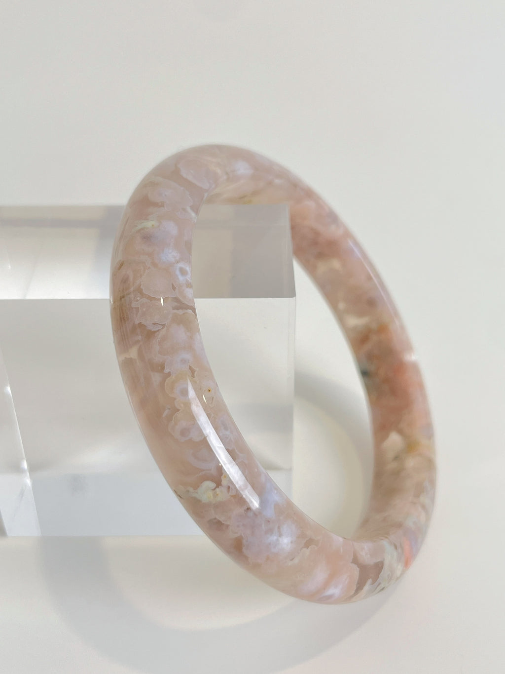 Beautiful flower agate bangle with soft pink hues, displayed on a clear stand.