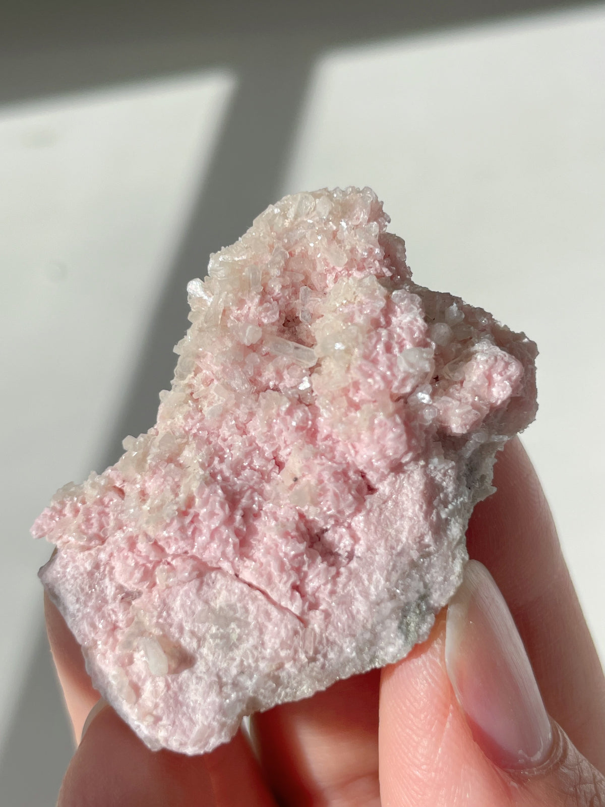 Rhodochrosite cluster with pink hues, showcasing sparkling crystal formations, held in a hand.