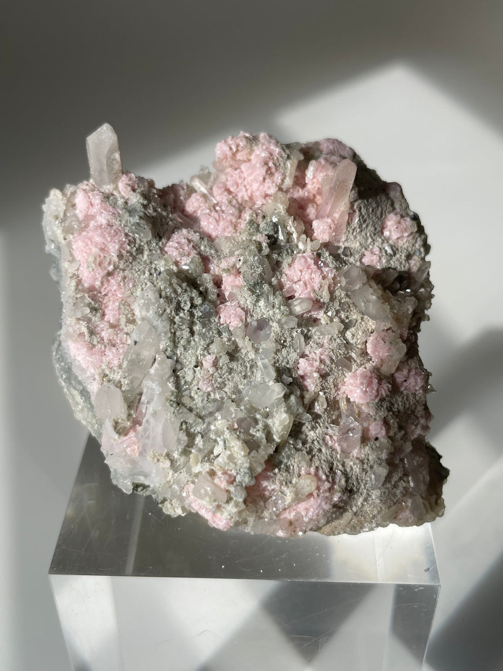 Rhodochrosite cluster with pink and gray hues, featuring clear crystal points, displayed on a clear stand.