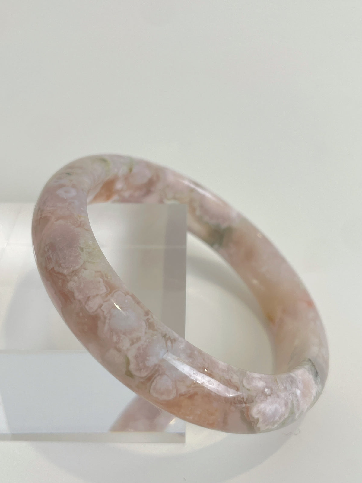 Beautiful flower agate bangle with soft pink hues, displayed on a clear stand.