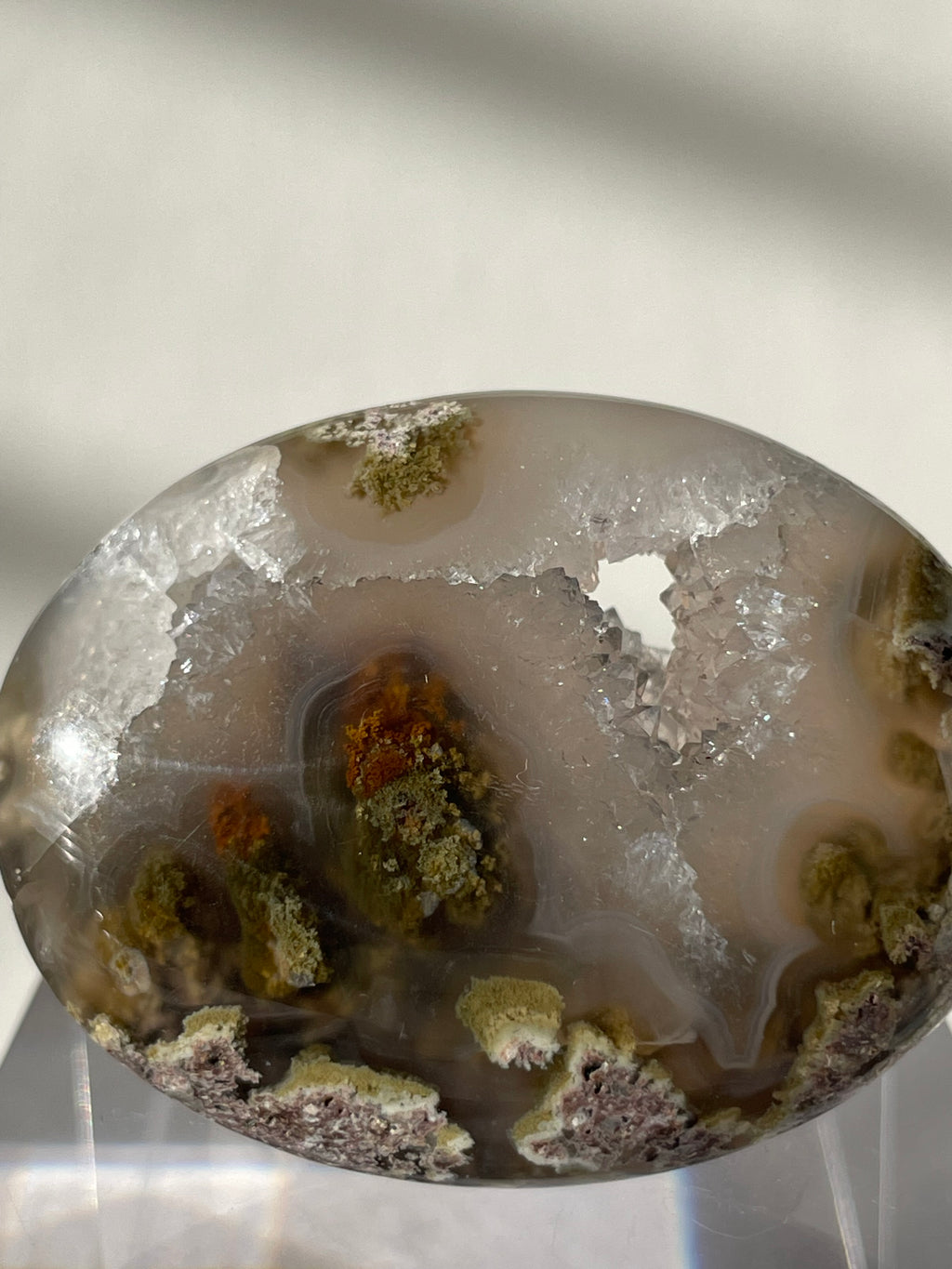 Scenic moss agate palm stone with earthy tones and unique patterns, displayed on a clear stand.