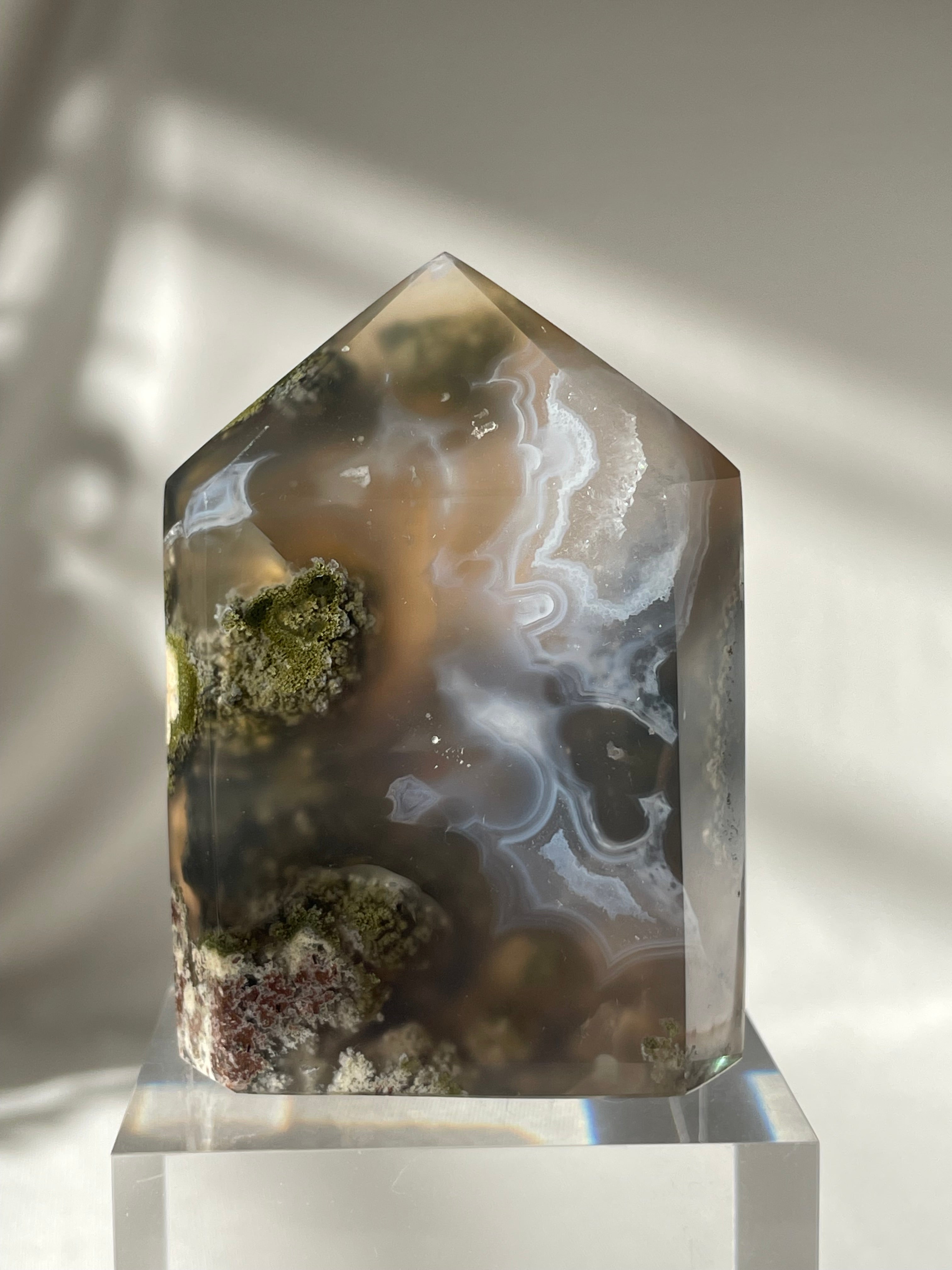 Scenic moss agate crystal tower with earthy tones and intricate patterns, displayed on a clear base.