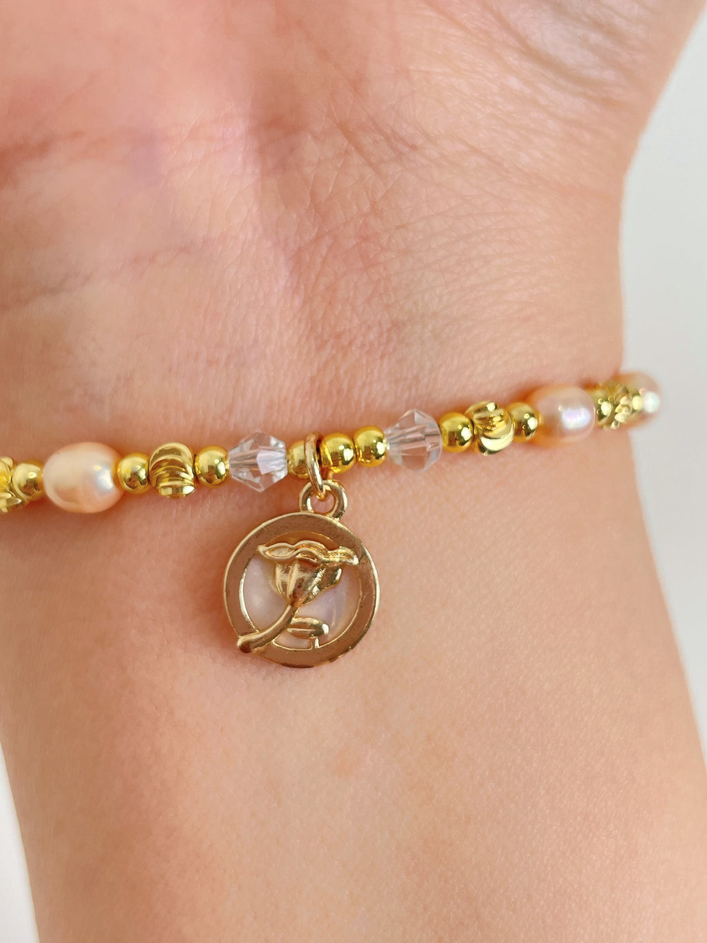 Delicate pink freshwater pearl bracelet with gold beads and a charm, elegantly worn on a wrist.