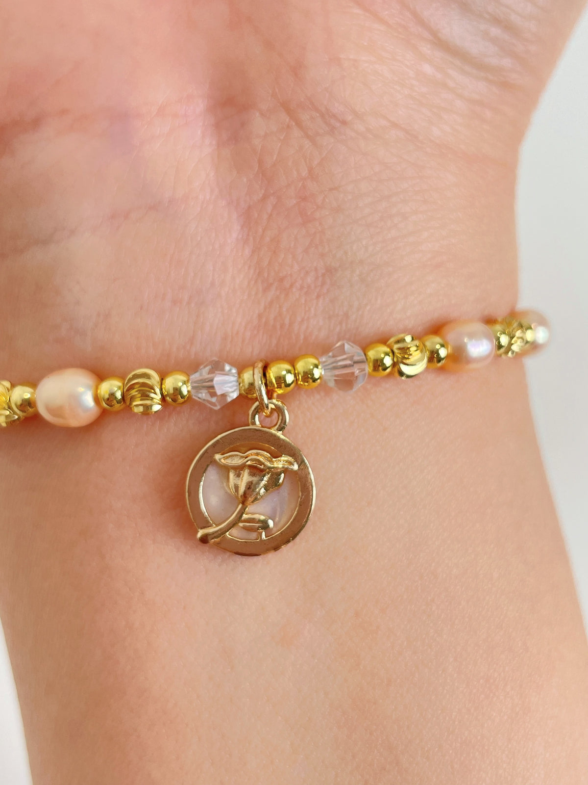 Delicate pink freshwater pearl bracelet with gold beads and a charm, elegantly worn on a wrist.