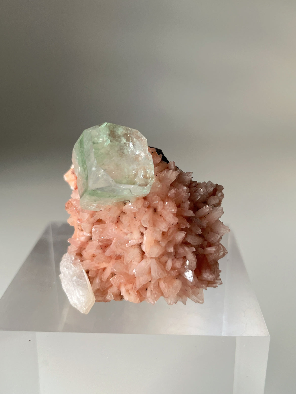 Beautiful pink Heulandite and Apophyllite crystal specimen displayed on a clear stand, showcasing its unique textures.