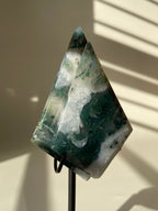 Scenic moss agate crystal specimen displayed on a stand, showcasing rich green and white patterns.