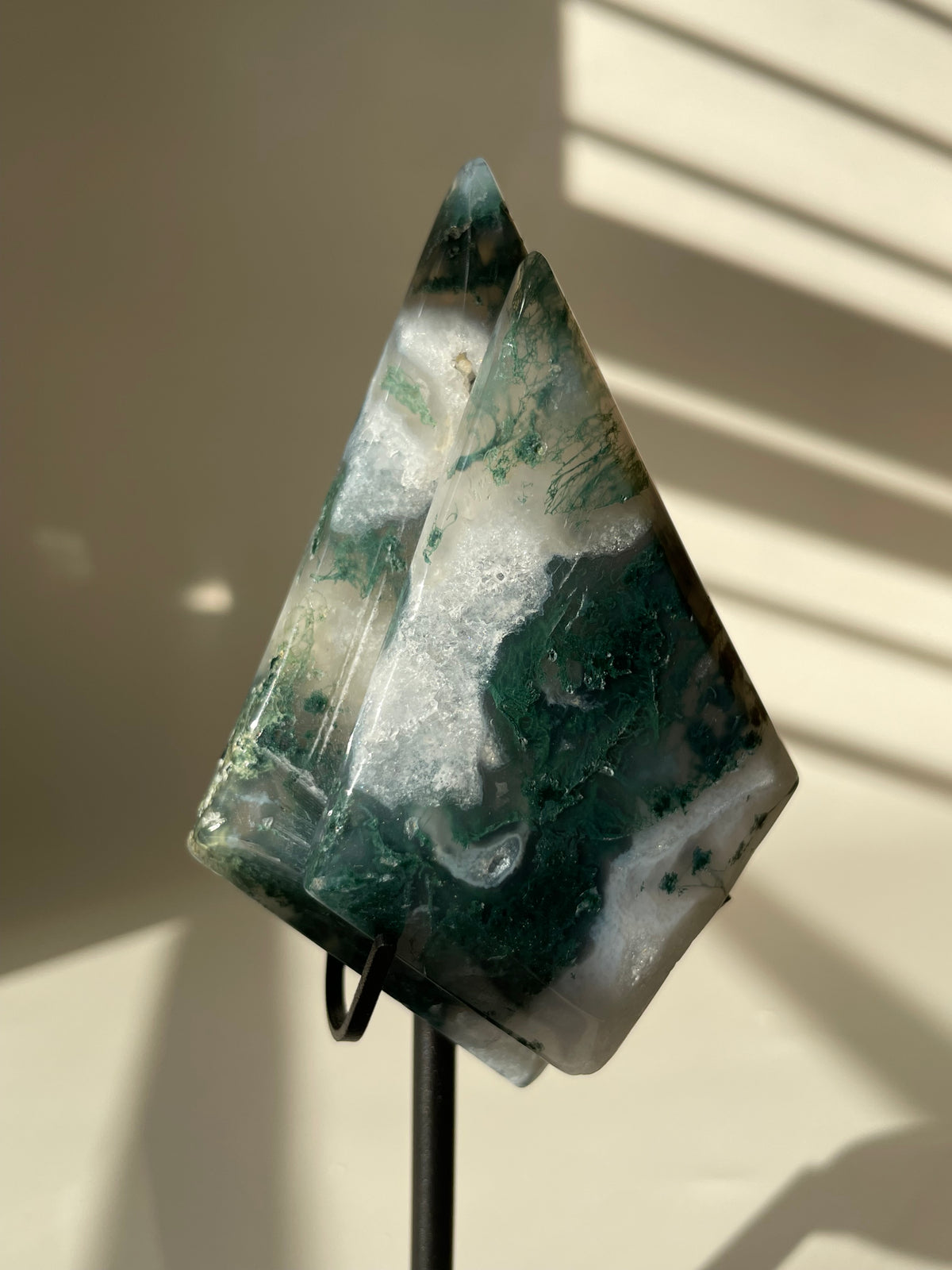 Scenic moss agate crystal specimen displayed on a stand, showcasing rich green and white patterns.