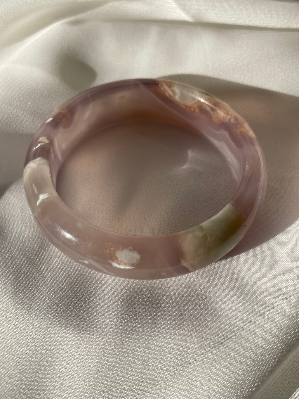Beautiful flower agate bangle with soft pink hues and natural patterns, resting on a light fabric background.