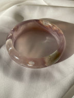 Beautiful flower agate bangle with soft pink hues and natural patterns, resting on a light fabric background.