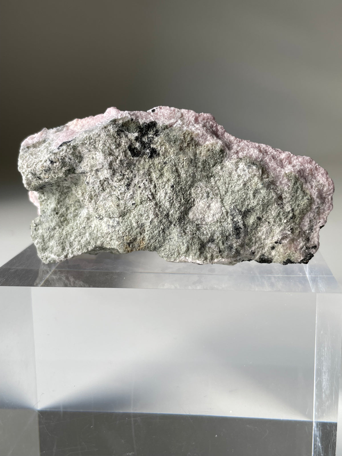 Rhodochrosite cluster with pink and gray hues, displayed on a clear acrylic stand, showcasing its natural beauty.