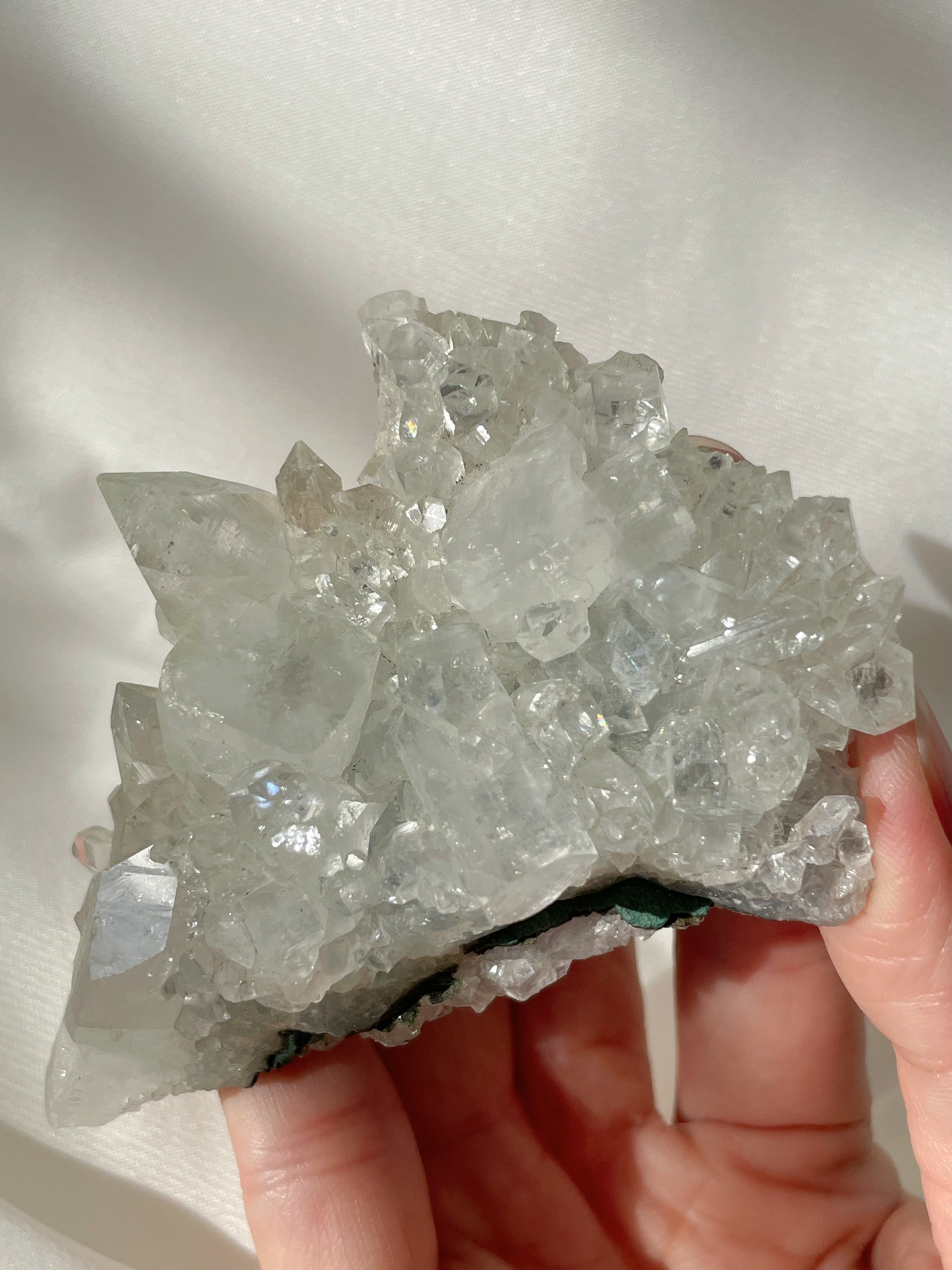 A hand holding a sparkling apophyllite cluster, showcasing its clear, crystalline formations and natural beauty.