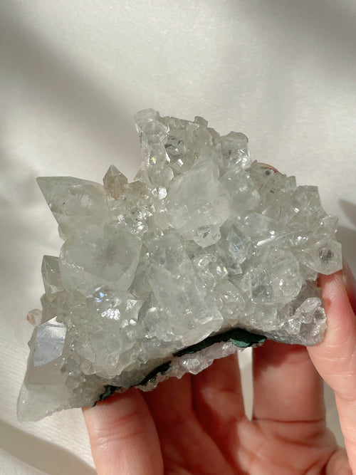 A hand holding a sparkling apophyllite cluster, showcasing its clear, crystalline formations and natural beauty.