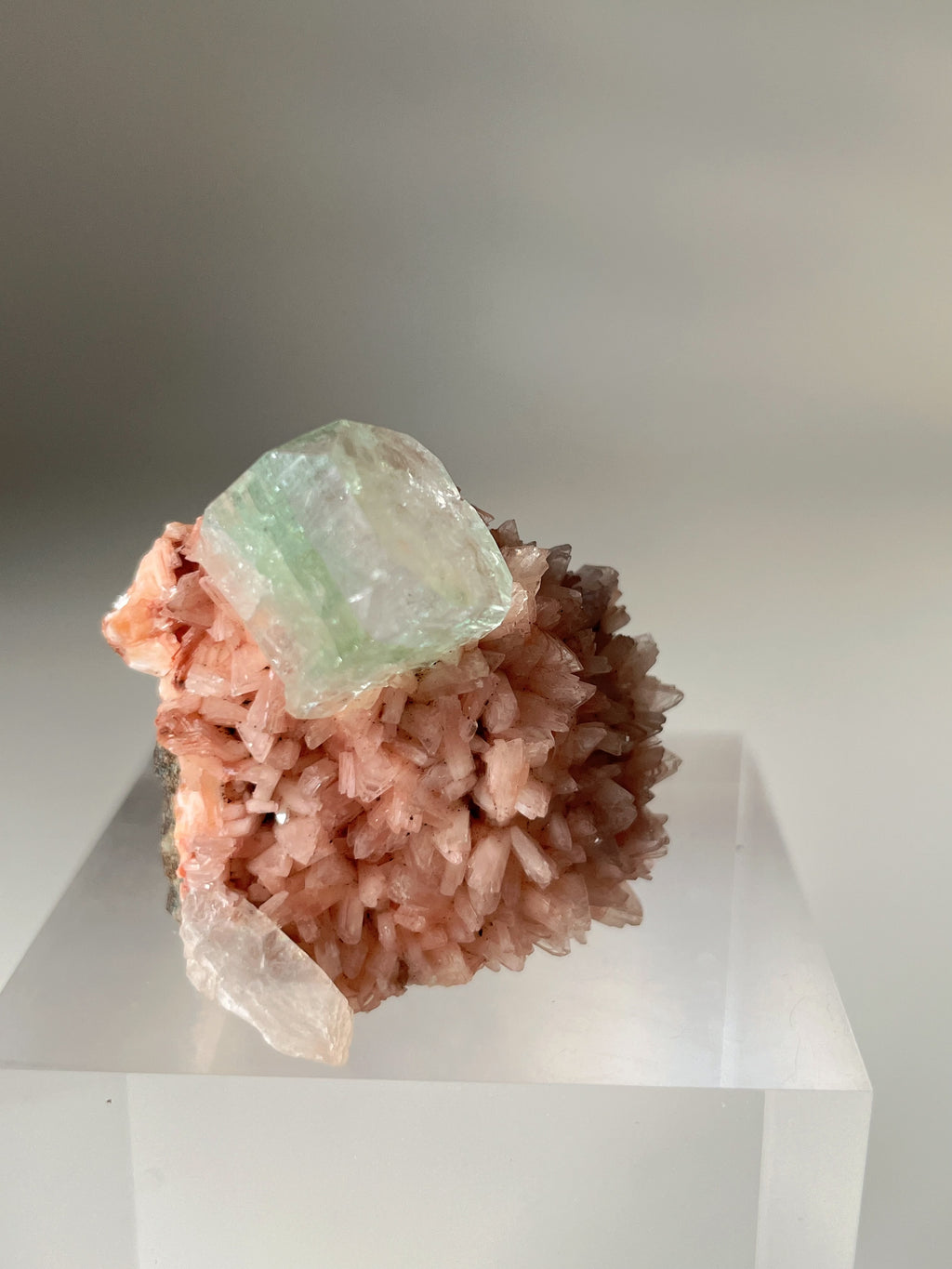 Pink Heulandite and Apophyllite crystal specimen with a textured surface, displayed on a clear stand.