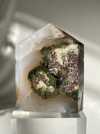 Scenic moss agate tower with earthy green and brown patterns, elegantly displayed on a clear base.