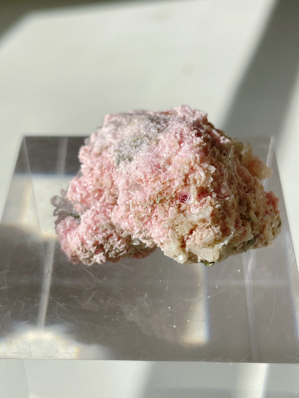 Rhodochrosite cluster with a soft pink hue, displayed on a clear stand, showcasing its natural crystal formations.