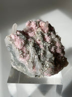 Rhodochrosite cluster with pink and gray hues, showcasing crystal formations on a clear display stand.