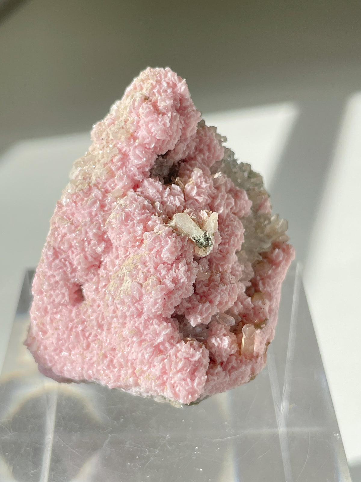 Rhodochrosite cluster with a textured pink surface, displayed on a clear stand, showcasing its natural beauty.