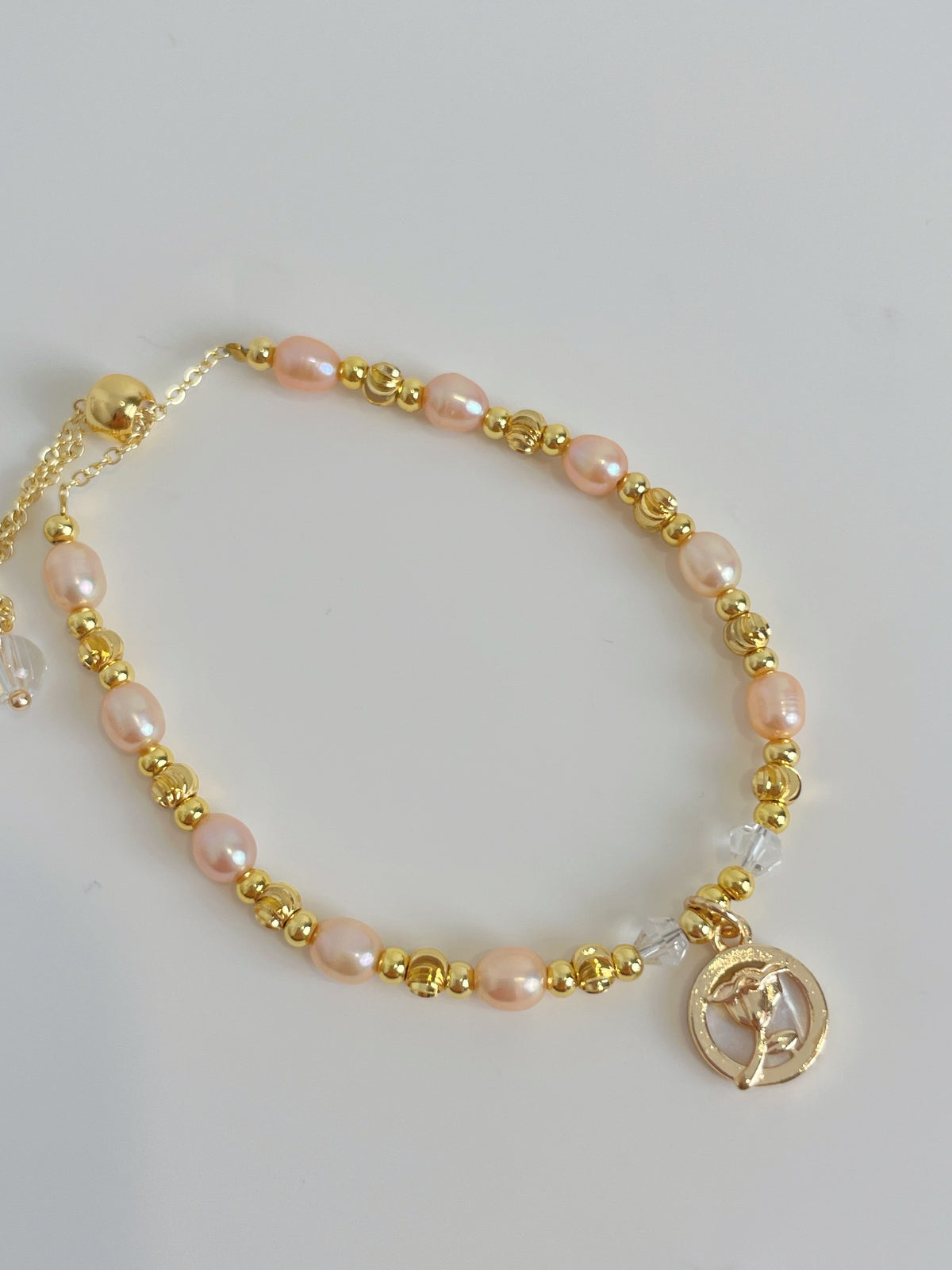 Delicate pink freshwater pearl bracelet with gold accents and a charm, perfect for elegant styling.