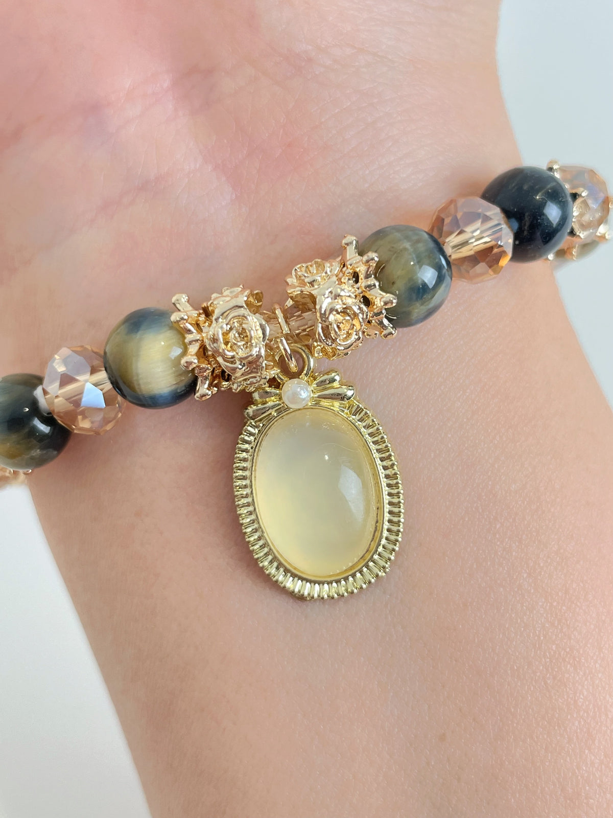 Elegant bracelet featuring blue tiger's eye beads and a gold pendant with floral accents.