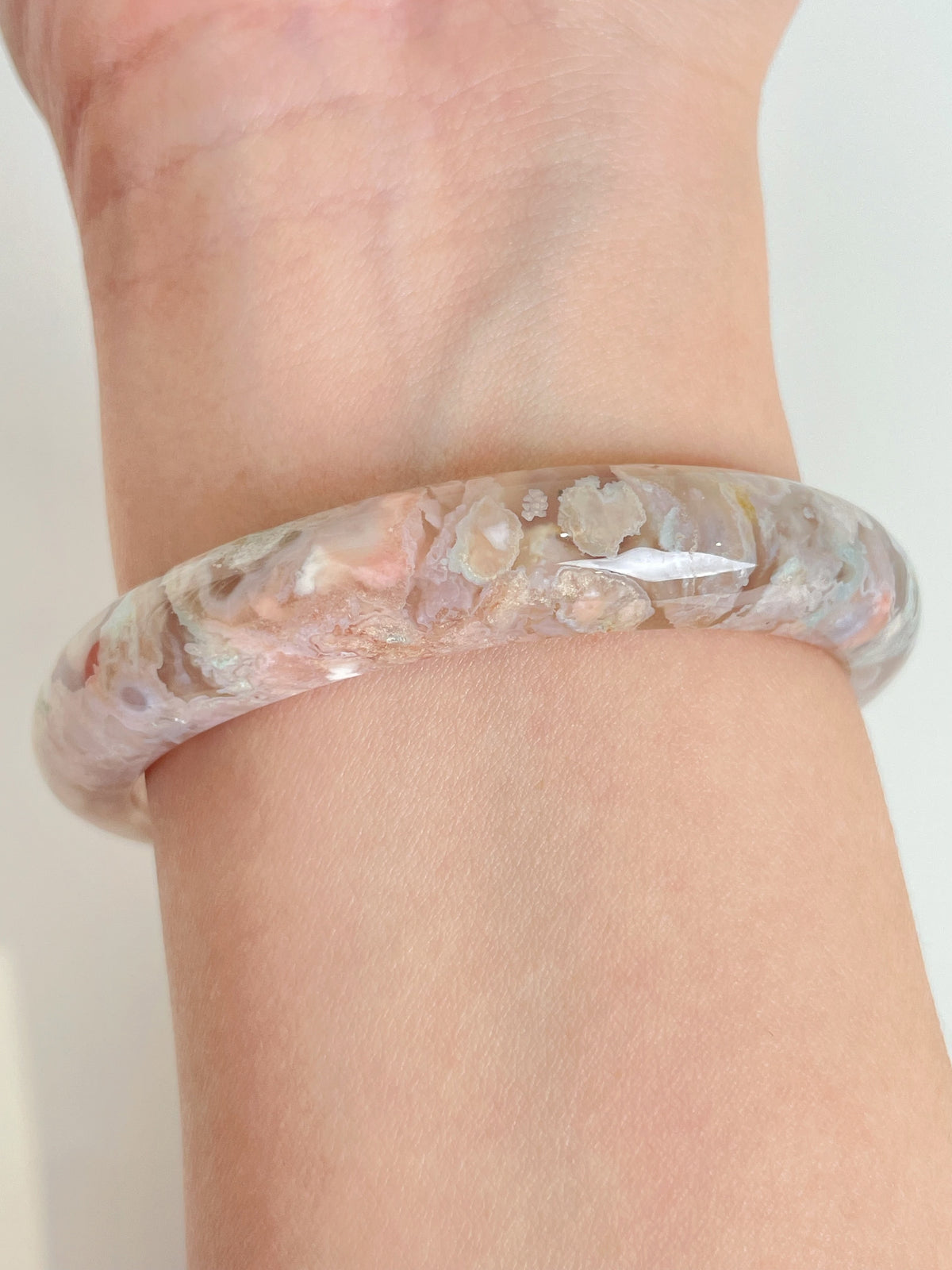 Beautiful flower agate bangle showcasing soft pink and cream hues, worn on a wrist.