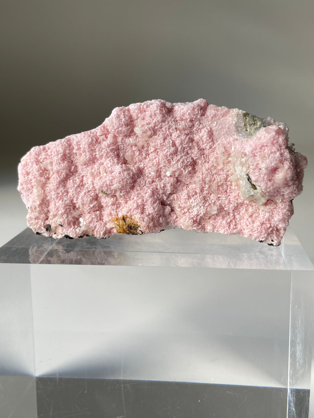 Rhodochrosite cluster with a soft pink hue, resting on a clear display stand, showcasing its natural texture.