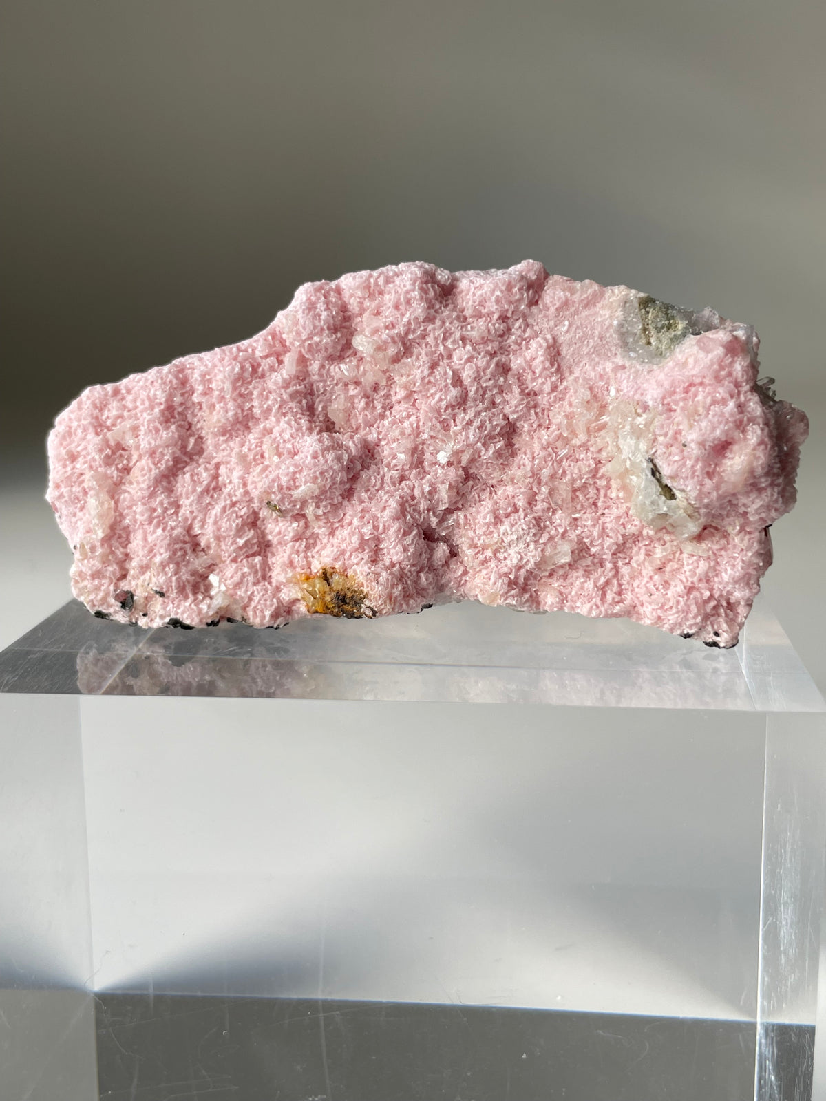 Rhodochrosite cluster with a soft pink hue, resting on a clear display stand, showcasing its natural texture.