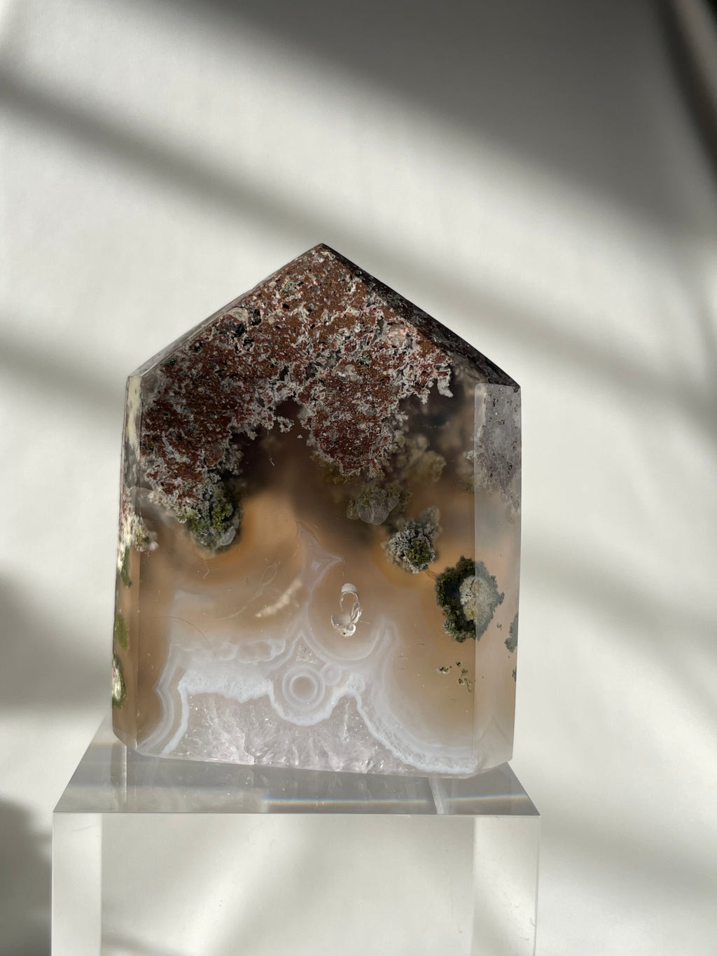 Scenic moss agate tower with earthy tones and unique patterns, displayed on a clear stand.