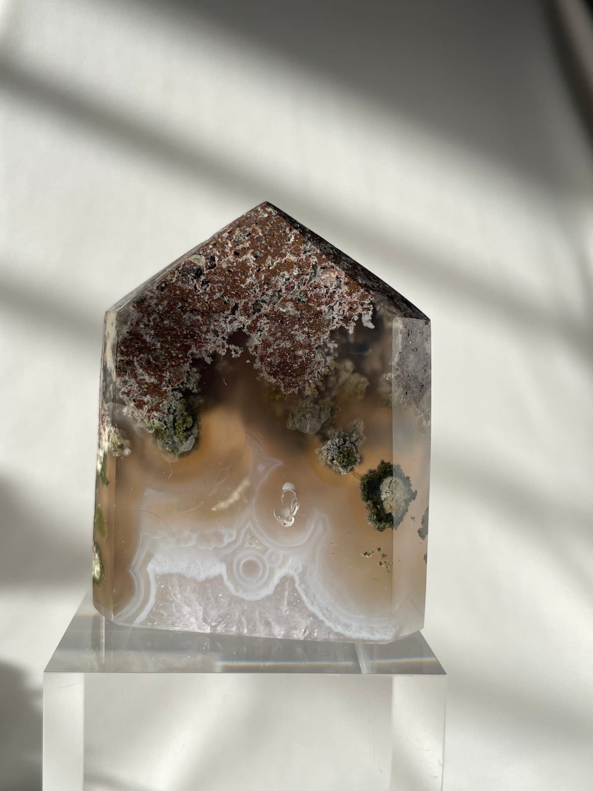 Scenic moss agate tower with earthy tones and unique patterns, displayed on a clear stand.