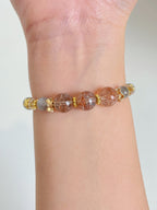 Rutilated quartz bracelet featuring 7-10mm beads with gold accents, worn on a wrist.