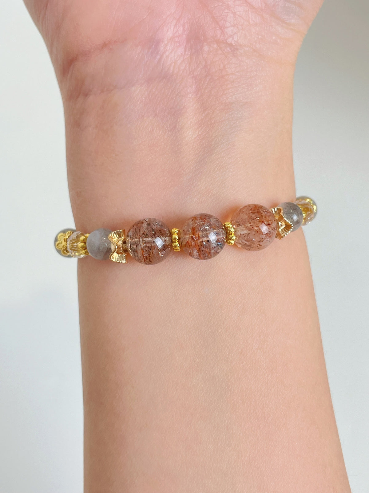 Rutilated quartz bracelet featuring 7-10mm beads with gold accents, worn on a wrist.