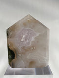 Scenic moss agate tower with soft pink and earthy tones, displayed on a clear stand, showcasing its unique patterns.