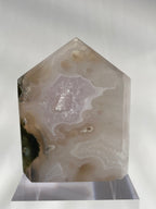 Scenic moss agate tower with soft pink and earthy tones, displayed on a clear stand, showcasing its unique patterns.