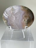 Scenic moss agate palm stone displayed on a clear stand, showcasing its unique patterns and colors.