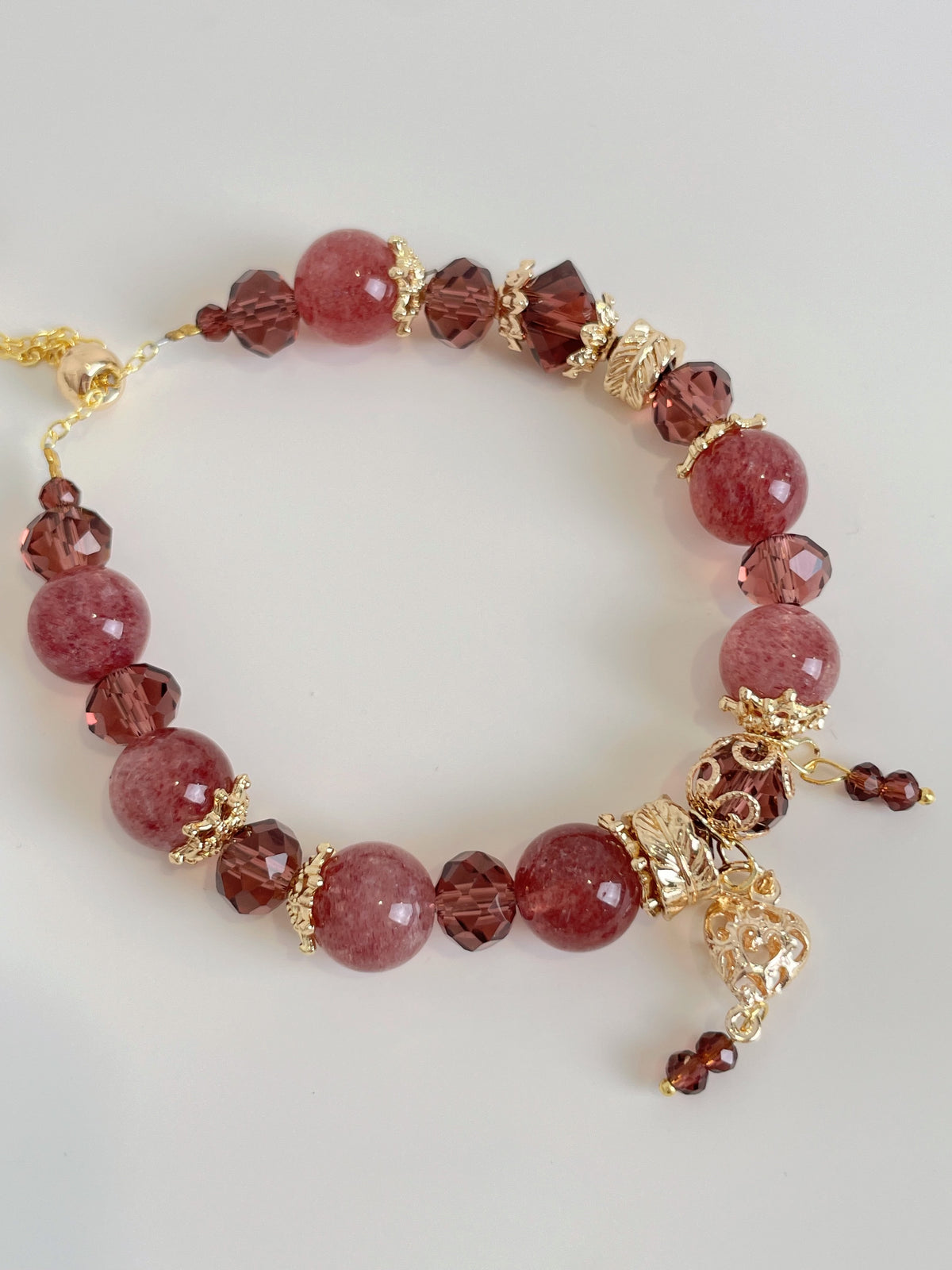 Strawberry quartz bracelet featuring 10mm beads, accented with gold and dark red crystals for a stunning look.