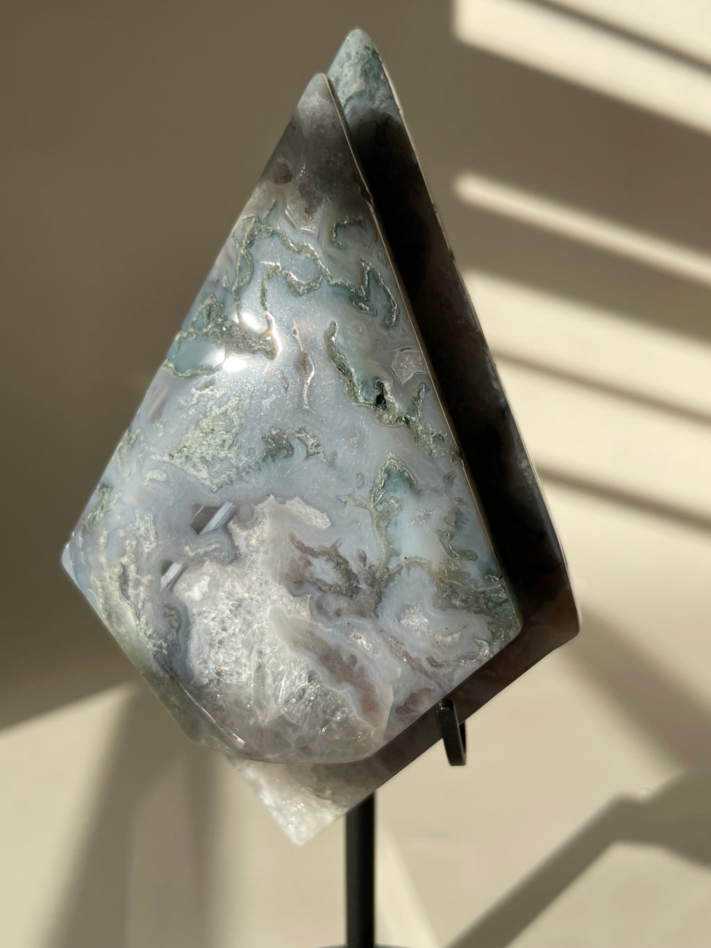 Scenic moss agate crystal specimen displayed on a stand, showcasing its unique patterns and colors.