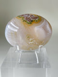Scenic moss agate palm stone with earthy tones and intricate patterns, displayed on a clear stand.