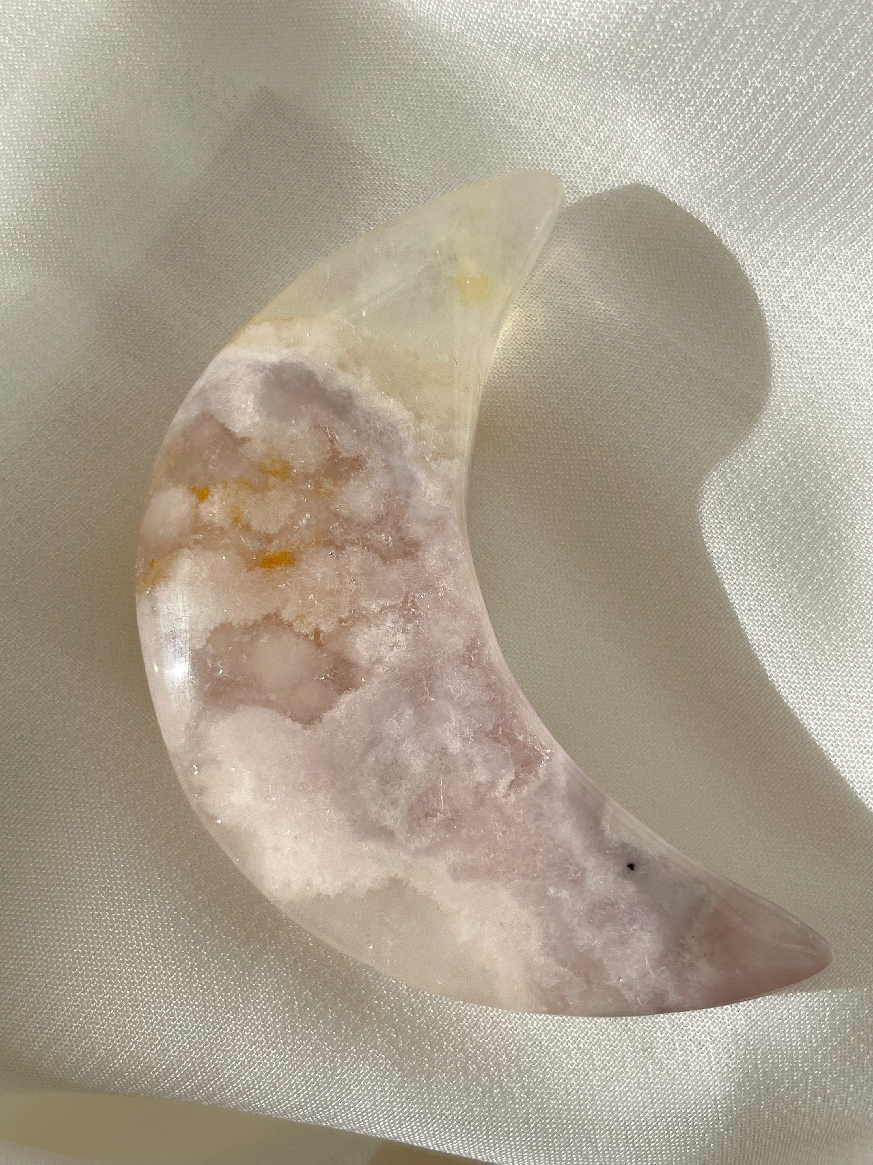 Beautiful flower agate moon with soft pink and white hues, resting on a light fabric background.