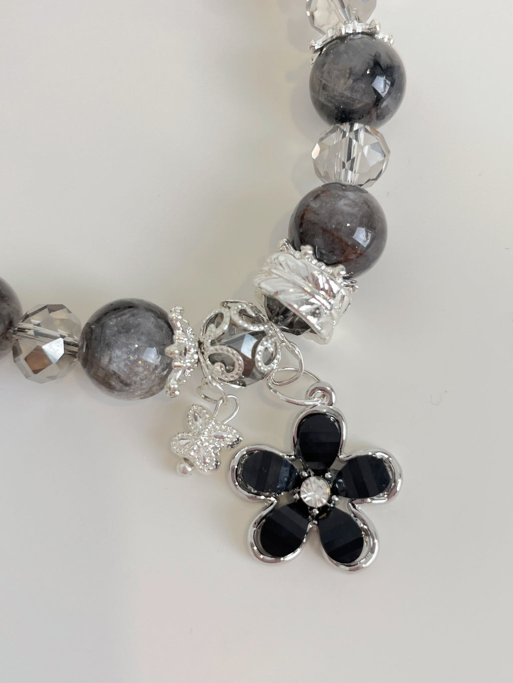 Beautiful quartz bracelet featuring a flower charm, accented with crystal and dark beads.