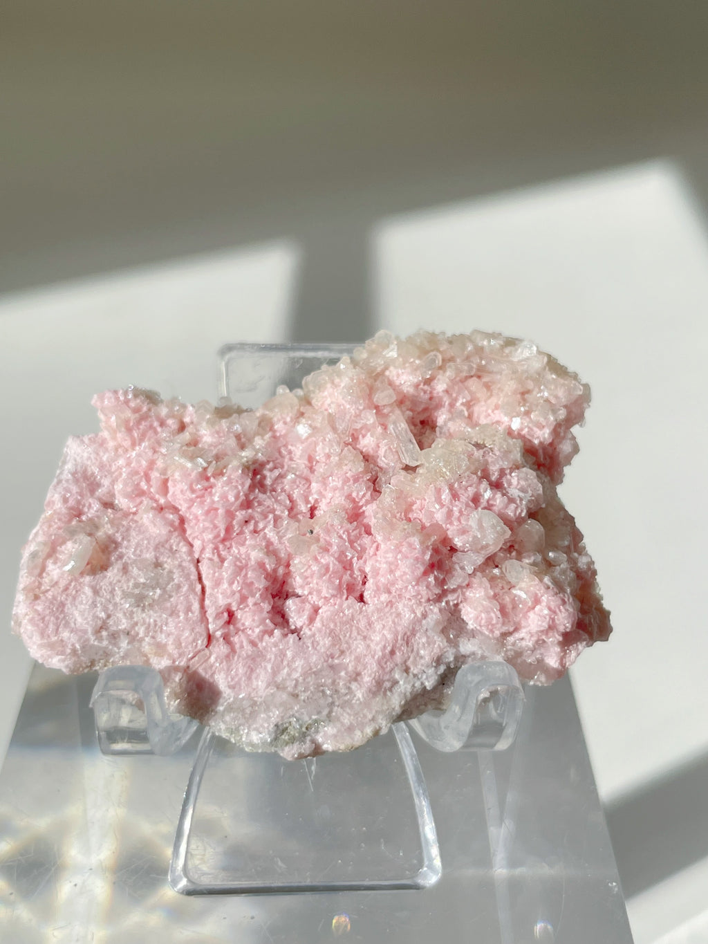 Beautiful rhodochrosite cluster with pink hues, displayed on a clear stand, showcasing its natural crystal formations.