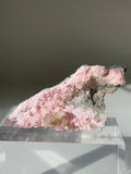 Beautiful rhodochrosite cluster with soft pink hues and natural textures, displayed on a clear stand.