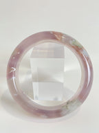 Beautiful flower agate bangle showcasing soft pink hues and natural patterns, displayed beside a clear cube.