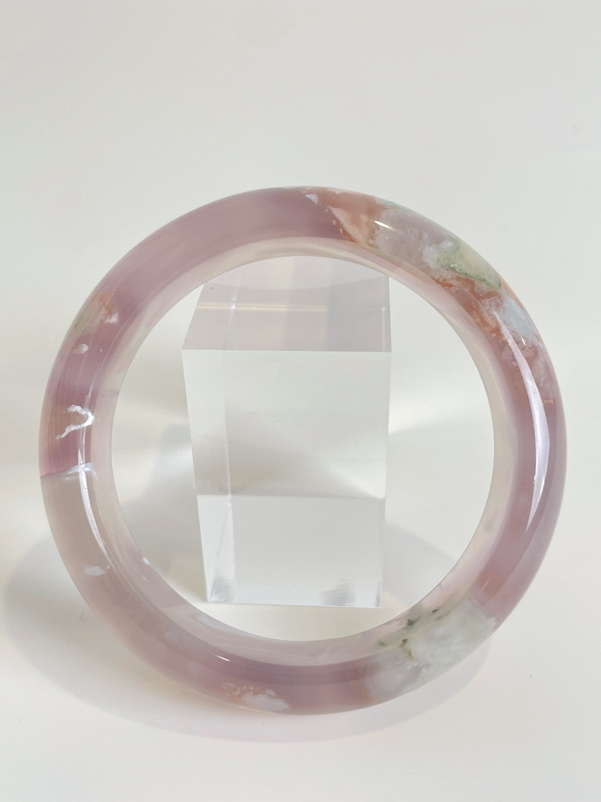 Beautiful flower agate bangle showcasing soft pink hues and natural patterns, displayed beside a clear cube.