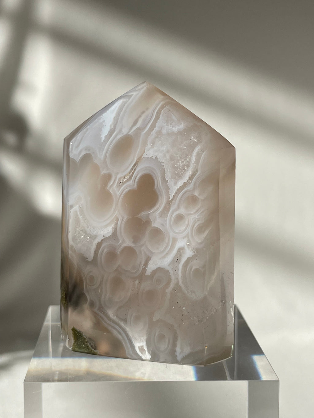 Scenic moss agate tower with soft, swirling patterns and a polished finish, resting on a clear display stand.