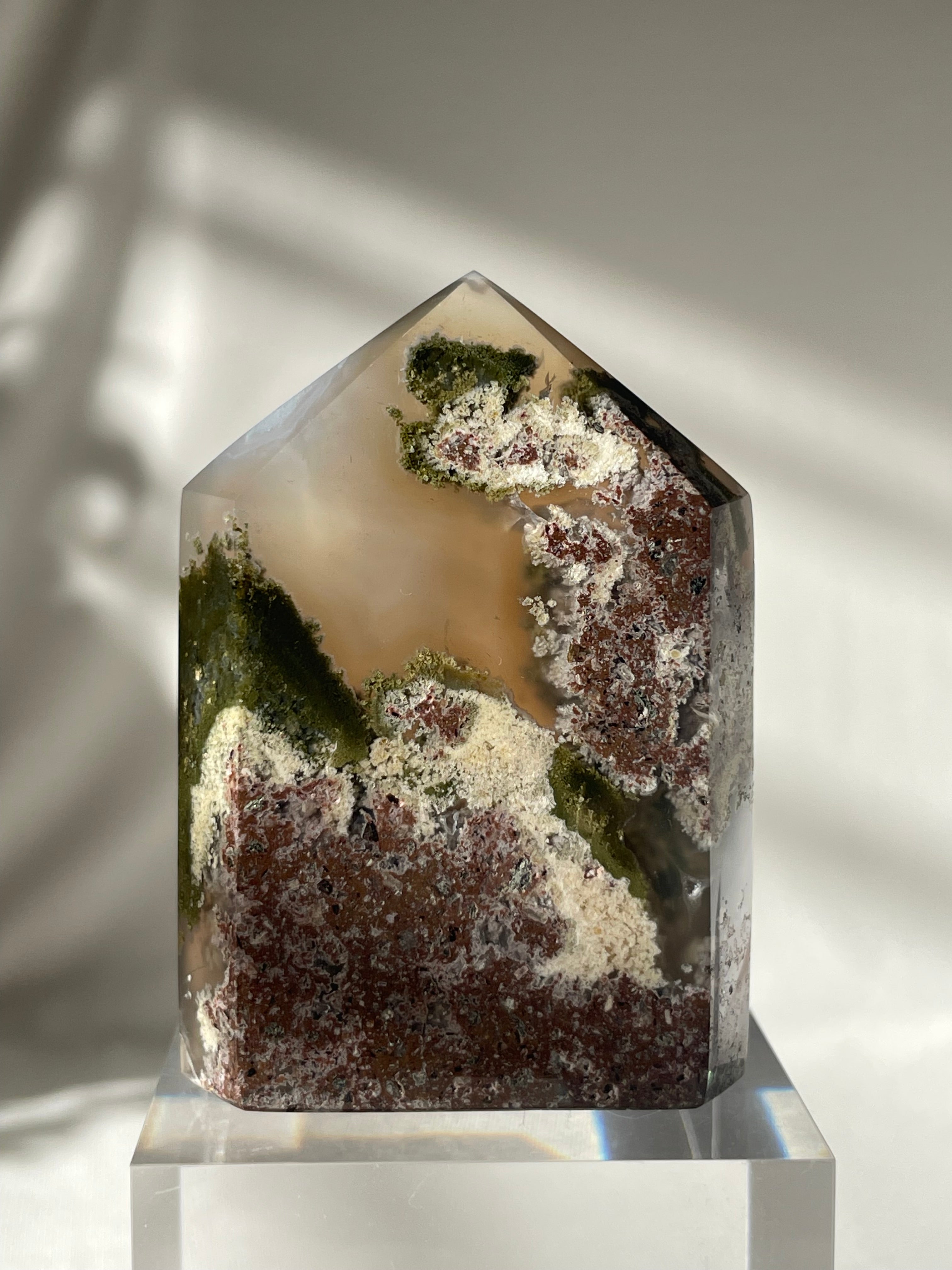 Scenic moss agate tower with earthy tones and natural patterns, displayed on a clear base.