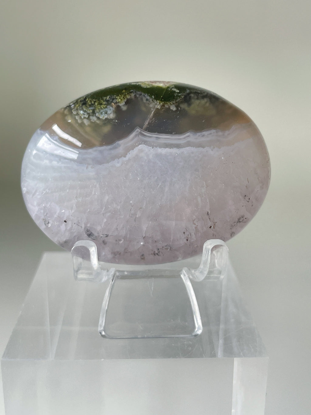 Scenic moss agate palm stone displayed on a clear stand, showcasing its unique patterns and colors.