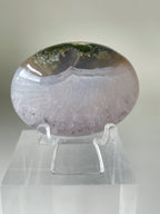 Scenic moss agate palm stone displayed on a clear stand, showcasing its unique patterns and colors.