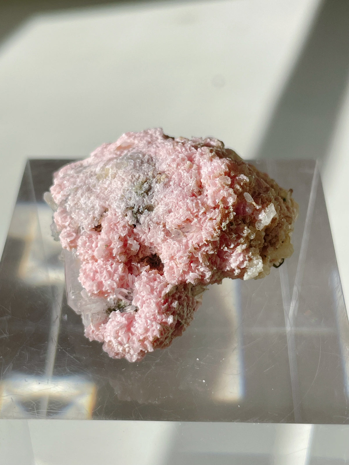 Beautiful rhodochrosite cluster with pink hues resting on a clear display stand, showcasing its unique texture and form.